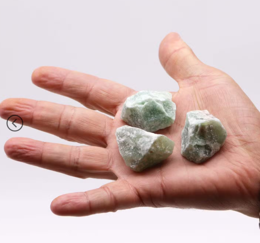 Three rough green crystal stones held in the open palm of a hand against a plain light gray background.