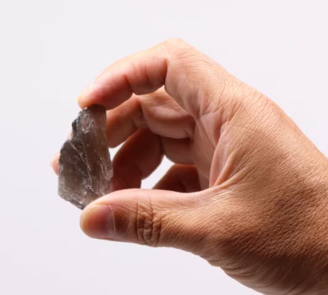 A hand holding a small, rough, translucent gray stone or crystal against a plain white background.
