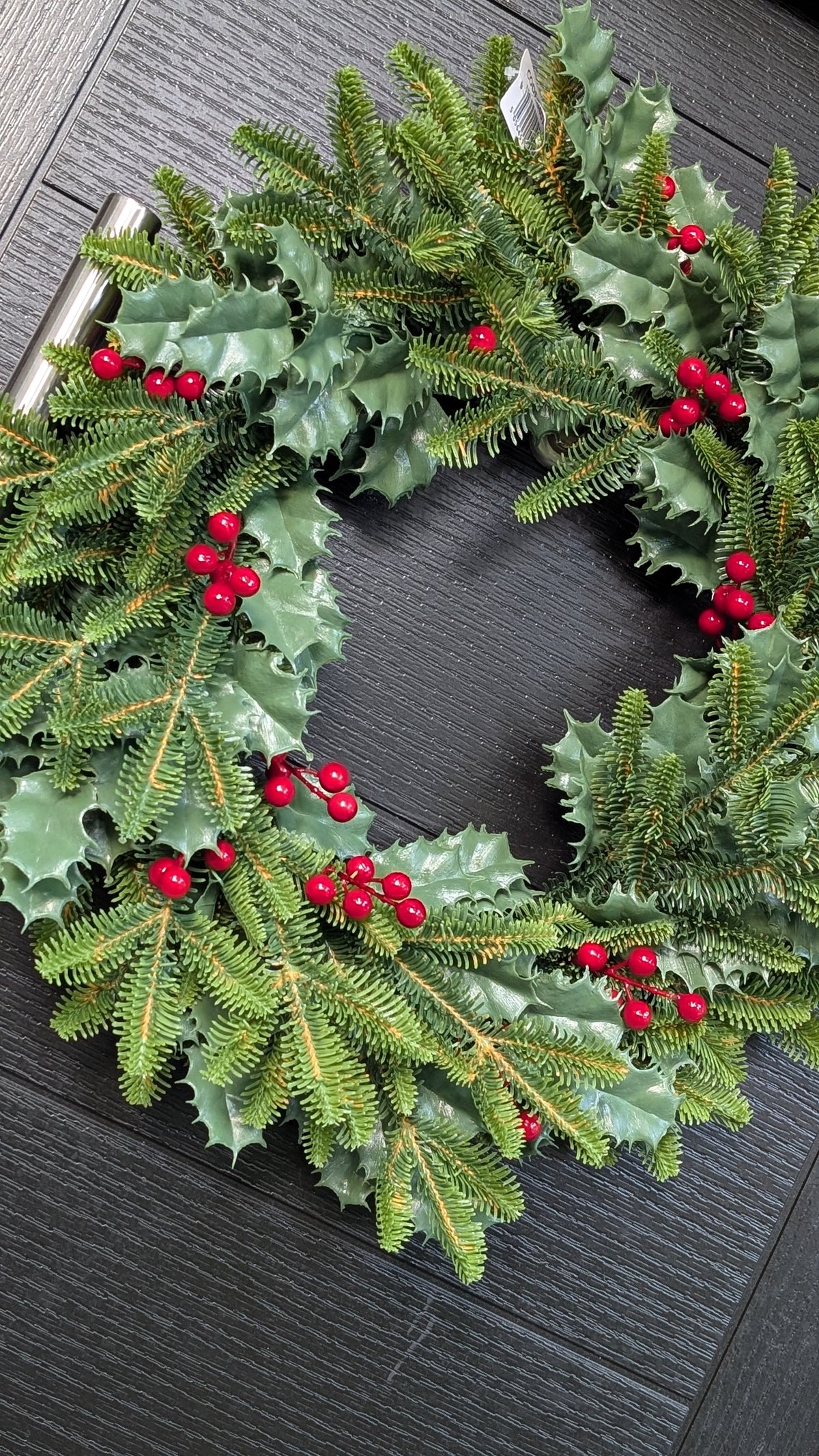 Approximate 60cm traditional Christmas wreath with green spruce foliage, glossy holly leaves and bright red berries displayed on a dark front door.