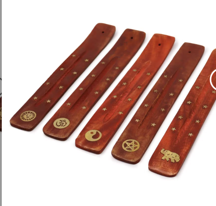 Five reddish-brown wooden incense sticks with gold-colored engraved symbols, including a wheel, Om, yin-yang, pentagram, and elephant, arranged diagonally on a white background.