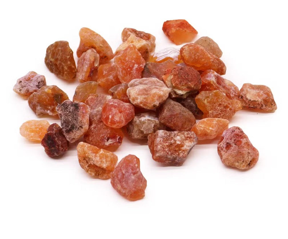 A pile of rough, unpolished orange and amber crystals, resembling raw salt or gemstone pieces, scattered on a plain white background.