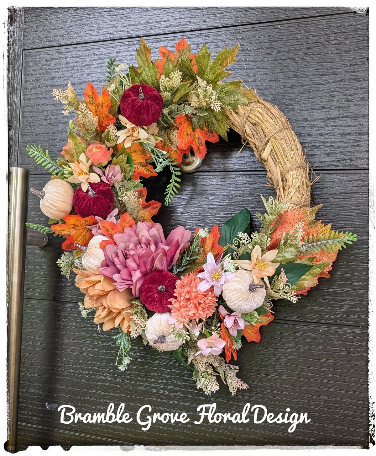 An autumn-themed floral wreath with faux pumpkins, chrysanthemums, and fall foliage, displayed on a dark gray wood-paneled door. The brand name 'Bramble Grove Floral Design' is printed in white text at the bottom.