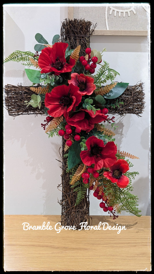 Handmade artificial red poppy floral cross on a rustic rattan base, decorated with red berries, green foliage and golden autumnal fern, by Bramble Grove Floral Design.