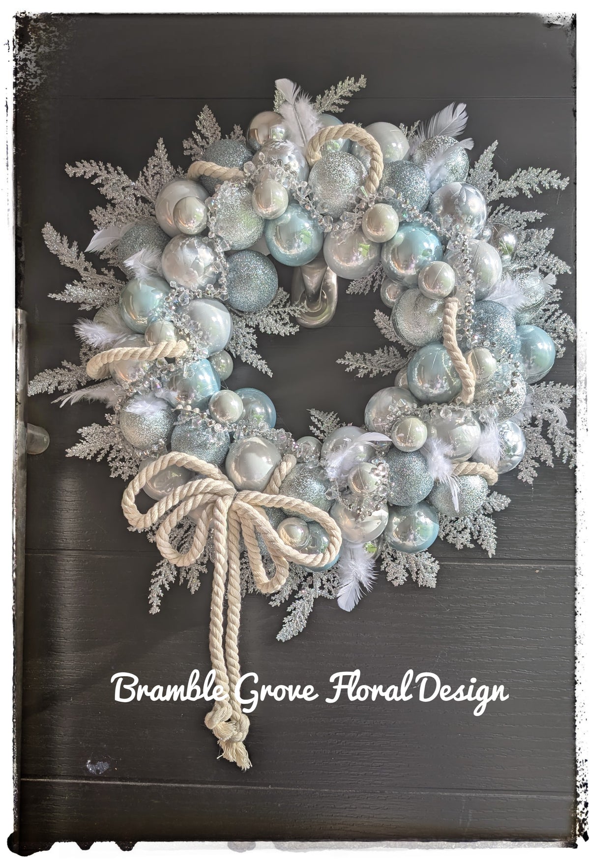 Luxury icy blue and silver Christmas wreath with crystal details, white feathers and ivory rope bow on a black door