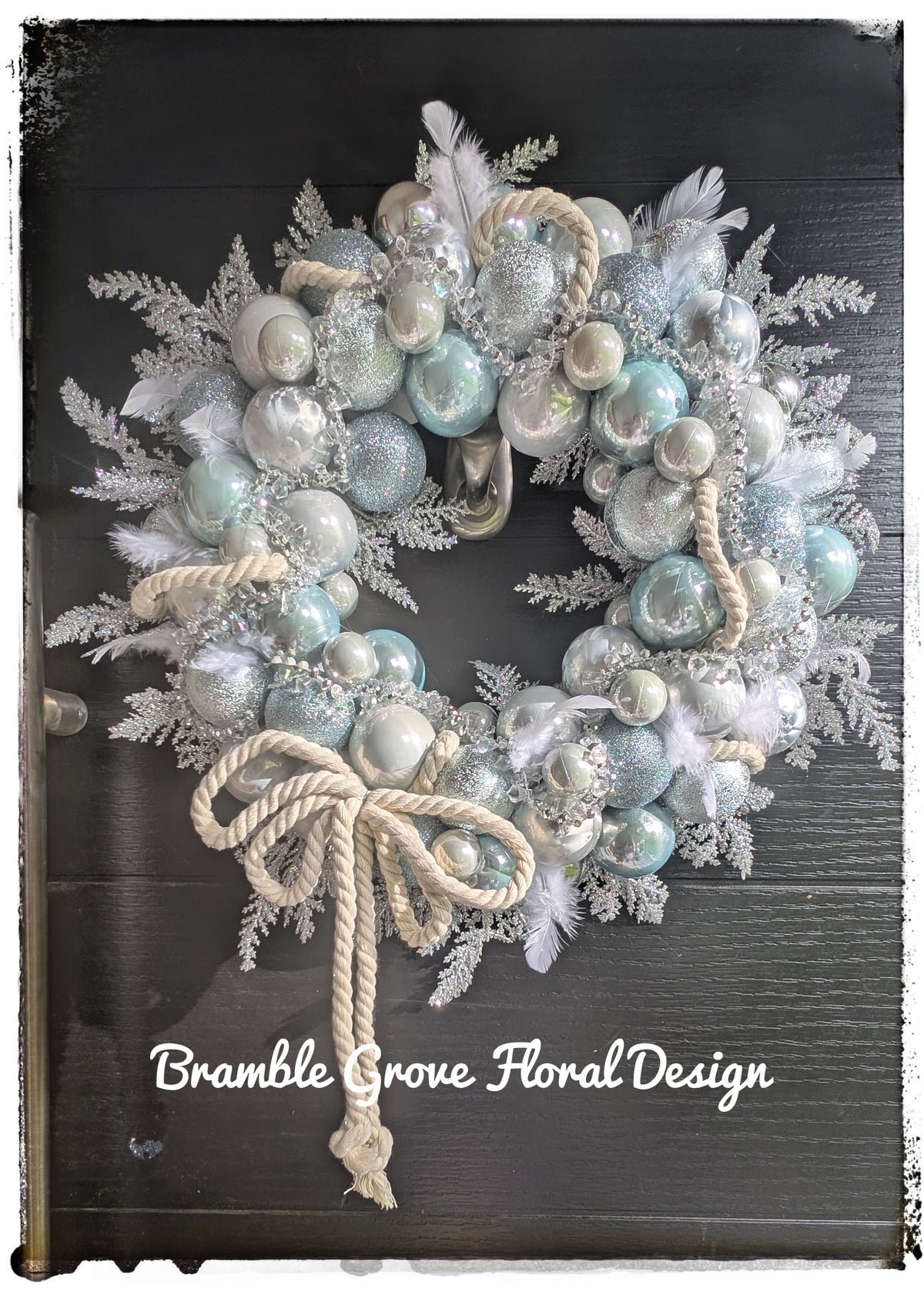Luxury icy blue and silver Christmas wreath with crystal details, white feathers and ivory rope bow on a black door