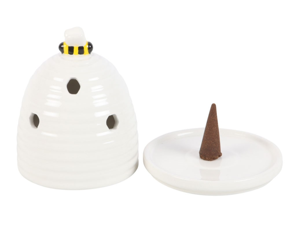 A white ceramic beehive-shaped incense burner with three ventilation holes, a small black and yellow accent ring near the top, a matching white lid, and a brown incense cone standing in the center of the dish, photographed on a white background.