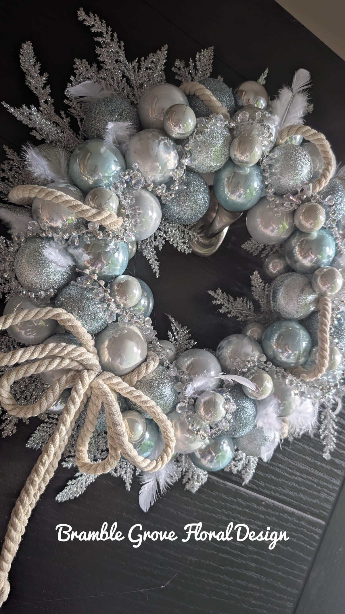 Luxury icy blue and silver Christmas wreath with crystal details, white feathers and ivory rope bow on a black door
