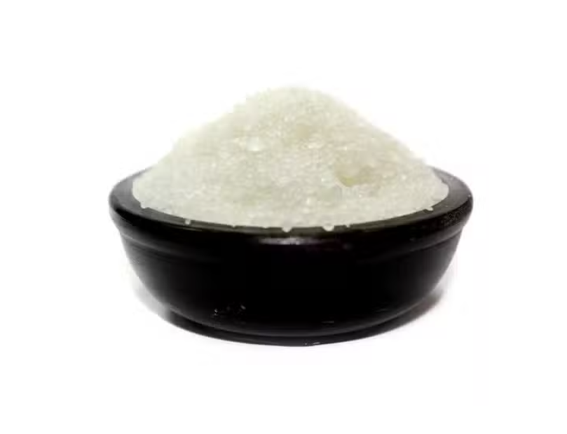A mound of coarse white crystalline powder, such as sugar or salt, presented in a small dark bowl against a plain white background.