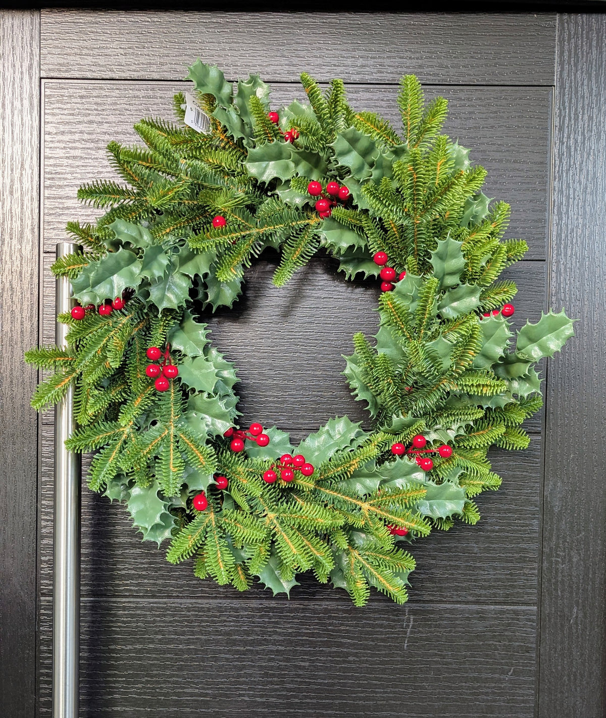 Approximate 60cm traditional Christmas wreath with green spruce foliage, glossy holly leaves and bright red berries displayed on a dark front door.