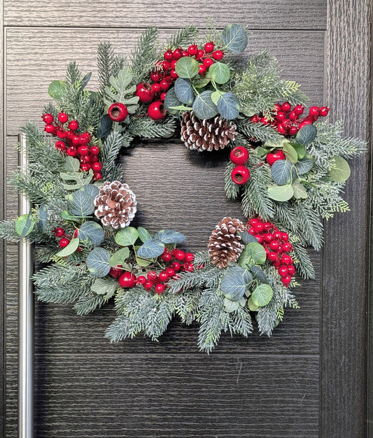 55cm traditional Christmas wreath featuring frosted evergreen foliage, red berries, snowy pinecones and eucalyptus-style leaves against a dark front door.
