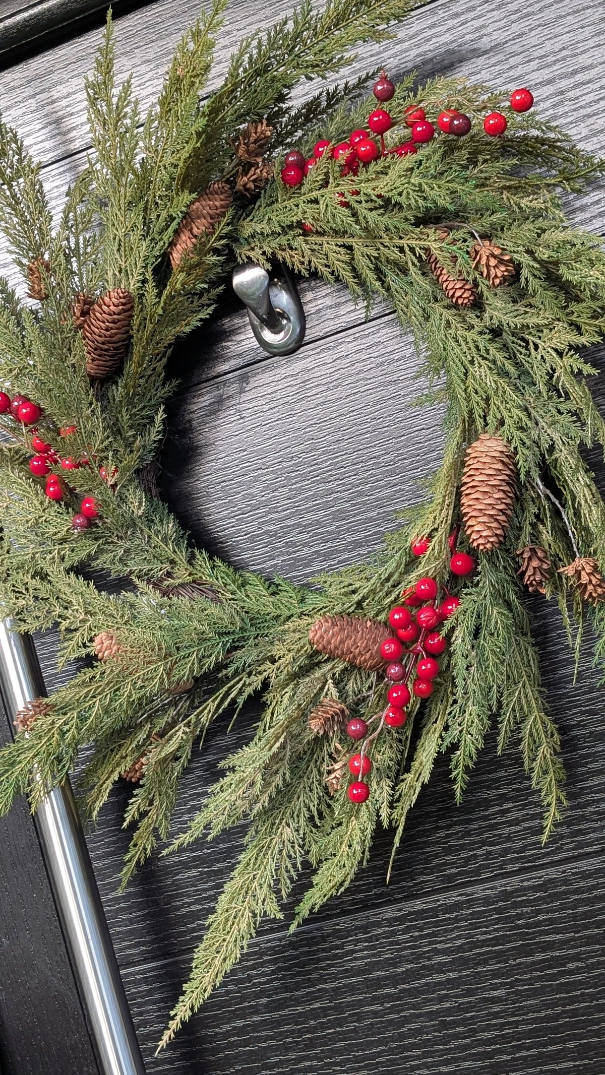 60cm ready-made Cupressus Christmas wreath with cascading green foliage, red berries and natural pinecones displayed on a dark front door.