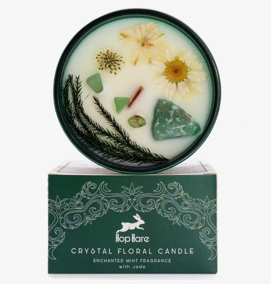 A top-down view of a Hopliare Crystal Floral Candle in a round dark green tin, showing pressed flowers and crystals in the wax, with its green patterned box below on a white background.