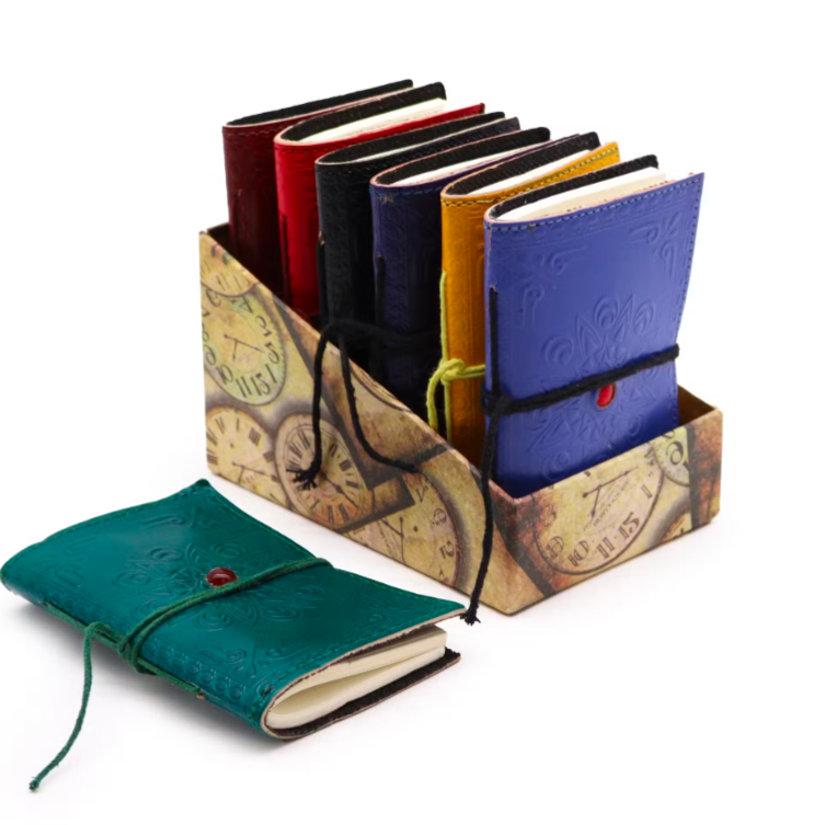 A set of small embossed leather journal notebooks displayed in a decorative cardboard holder, with one teal notebook placed in front on a white background.
