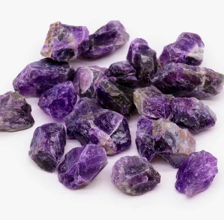 A pile of rough, unpolished purple amethyst stones on a clean white background.