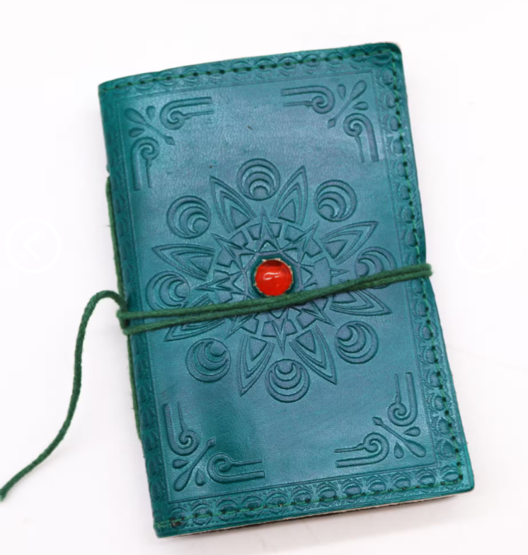 A teal leather journal with embossed mandala and scroll patterns, secured with a green cord and a red button, on a white background.