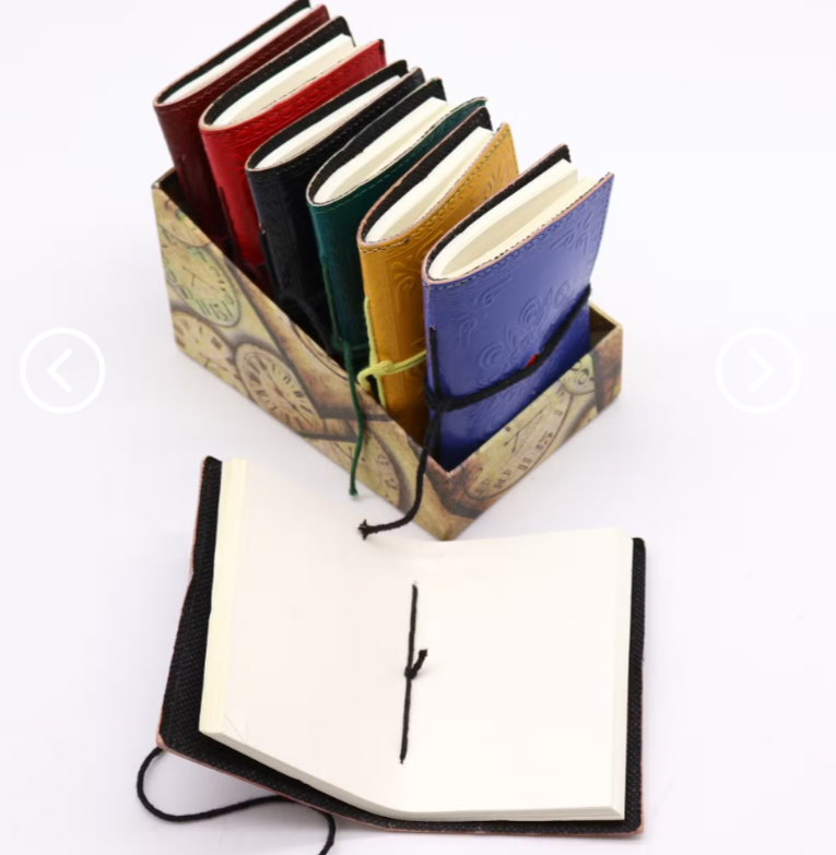 A set of colorful leather-bound notebooks displayed in a decorative holder, with one notebook shown open in front on a white background.