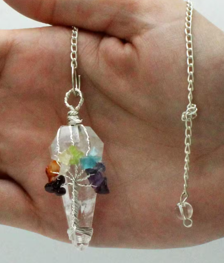 A silver chain necklace with a clear crystal coffin pendant containing small multicolored gemstone chips, held in a person's hand.